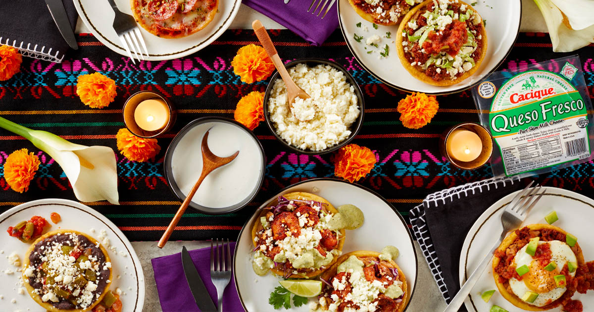 Table with an array of tacos, cheeses, and cremas, with a mexican blanket and orange flowers